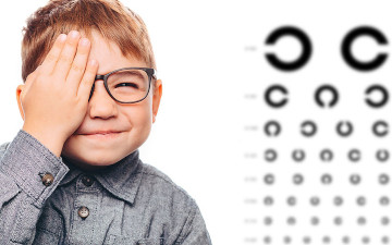 Kind mit Brille neben einer Tafel, um bei der Vorsorge in der Sehschule der Augenpartner auf Sehstörungen zu untersuchen 