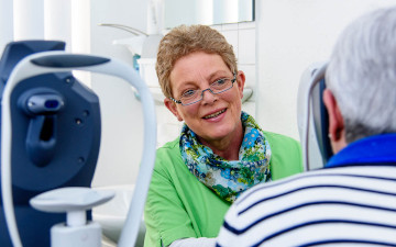 Eine Mitarbeiterin vor der Untersuchung einer Seniorin optische Kohaerenztomografie