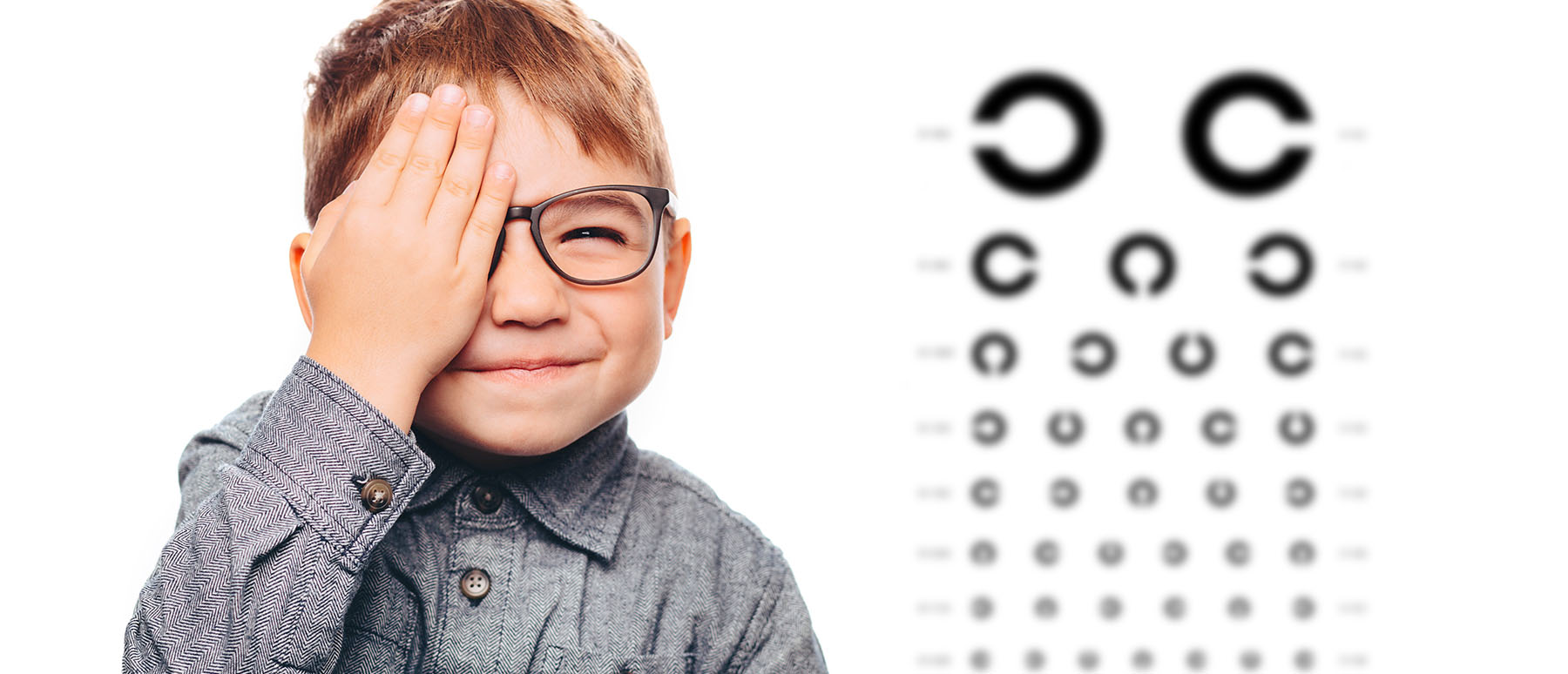 Kind mit Brille neben einer Tafel, um bei der Vorsorge in der Sehschule der Augenpartner auf Sehstörungen zu untersuchen 